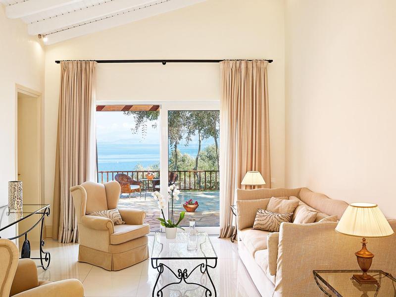 Salon lumineux avec mobilier beige et vue sur la mer par la porte-fenêtre ouverte.