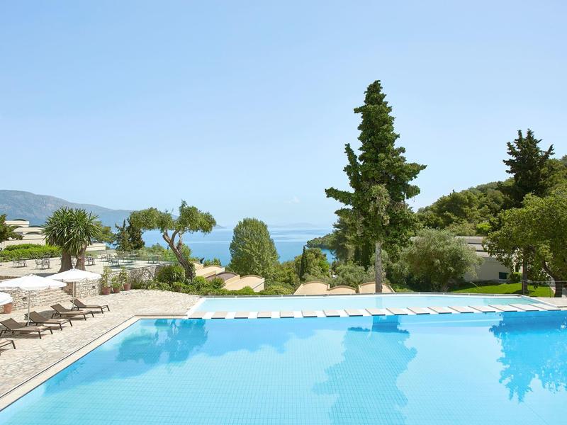 Piscine avec chaises longues donnant sur la mer et le paysage verdoyant sous un ciel clair