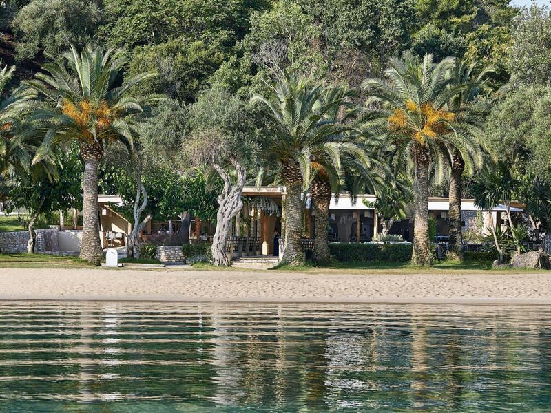 Zone de plage avec des palmiers et des bâtiments d'hôtel en arrière-plan près d'une eau calme.