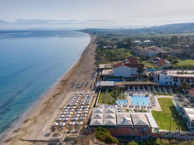 Luftaufnahme eines Strandes mit Liegestühlen, angrenzendem Poolbereich und Hotelgebäuden.
