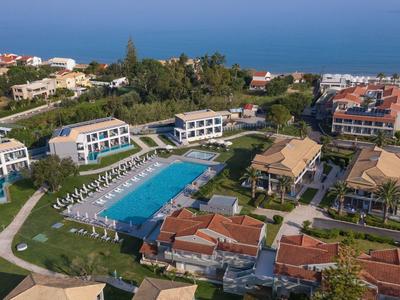 Luftaufnahme eines Ferienresorts mit großem Pool, grünen Wiesen und Meer im Hintergrund.