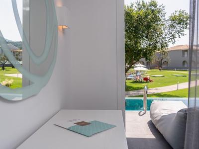 Moderner Außenbereich mit weißem Tisch, rundem Spiegel, Betten und Blick auf Garten und Pool.