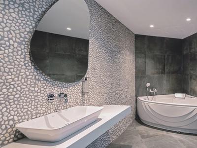 Moderne graue Badgestaltung mit großer runder Spiegelwand und eckigen Waschbecken, Eckbadewanne.