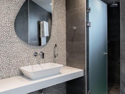 Modernes Badezimmer mit ovalem Spiegel, weißem Waschbecken und Dusche mit Milchglaswand.