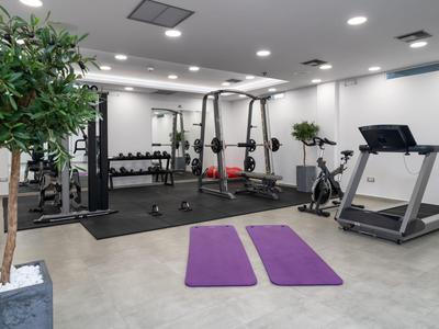 Moderner Fitnessraum mit Hanteln, Laufband, zwei lila Yogamatten und grünen Pflanzen.