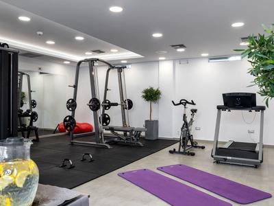 Moderner Fitnessraum mit Gym-Geräten, zwei Yogamatten, hellen Wänden und grünen Pflanzen.