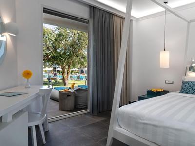 Modernes, helles Schlafzimmer mit großem Bett, Schreibtisch, Sitzecke und Terrasse mit Blick ins Grüne.