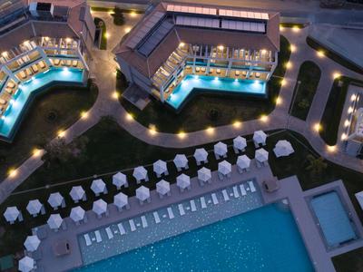 Vogelperspektive eines beleuchteten Hotels mit Pool, Sonnenliegen und Schirmen bei Nacht.
