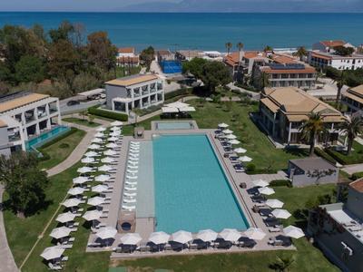 Moderner Hotelkomplex mit großem rechteckigem Pool, Liegestühlen und Blick auf das Meer.