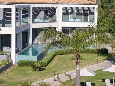 Modernes Hotel mit Pool, Palmen und gepflegtem Garten unter blauem Himmel.