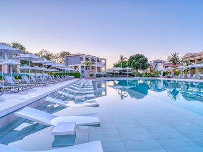 Moderner Hotelpool mit Sonnenliegen, Palmen und klarem Wasser bei Sonnenuntergang.