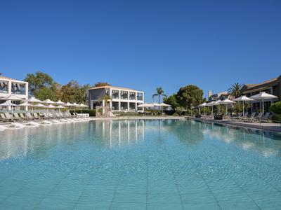 Großer Hotelpool mit Liegestühlen und klar blauem Himmel.