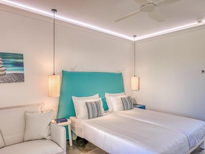 Modernes Hotelzimmer mit Doppelbett, türkisfarbenem Kopfteil und zwei Hängeleuchten.