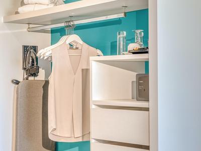 Moderner Hotelkleiderschrank mit türkisfarbener Wand, Bügelbrett, Kleidung und Schubladen.