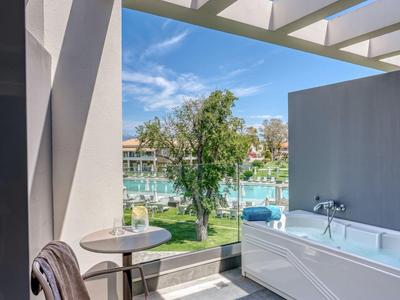Moderner Außenbereich mit Badewanne, Stuhl und Blick auf Wasser und Bäume unter blauem Himmel.
