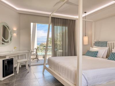 Helles Hotelzimmer mit Doppelbett, Schreibtisch, Minibar und Balkon mit Meeresblick.