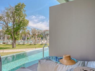 Moderner Hotelpool mit gemütlicher Liege, Kissen und beruhigendem Blick auf Bäume und Himmel.