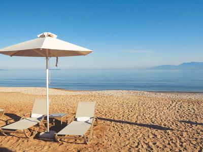 Strand mit goldenem Sand, zwei weißen Liegestühlen und großem Sonnenschirm bei klarem Himmel.