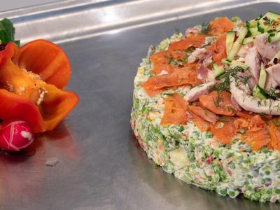 Runder Frischkäse mit Kräutern, Lachs und Schinken, daneben geschnittene Paprika und Radieschen.