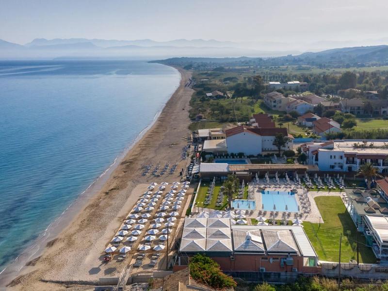 Hotelový areál s bazénem a slunečníky přímo u dlouhé písečné pláže a klidného moře.