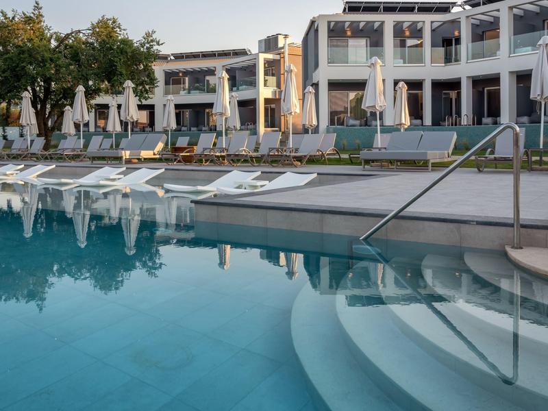 Moderní hotelový bazén s lehátky a slunečníky za jasné oblohy.