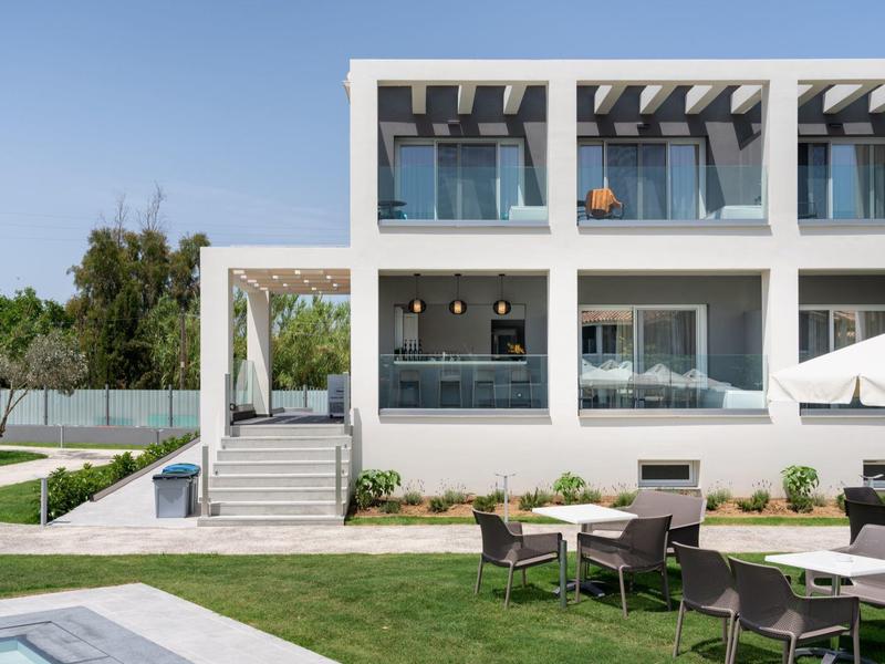 Moderní hotel s bílými budovami, terasou a zahradou za jasné oblohy.