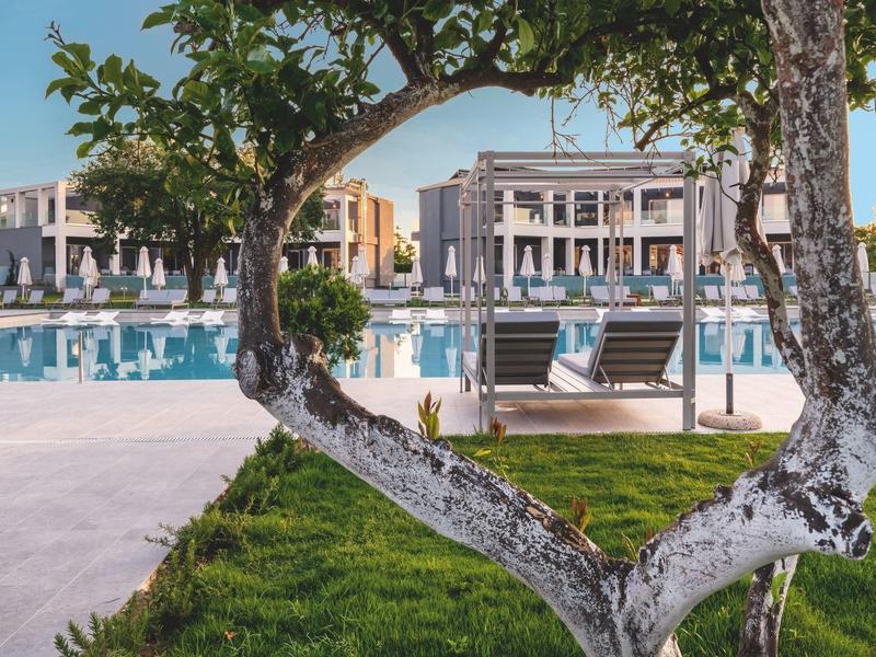 Budova hotelu s bazénem rámovaným stromem ve tvaru srdce a zeleným trávníkem