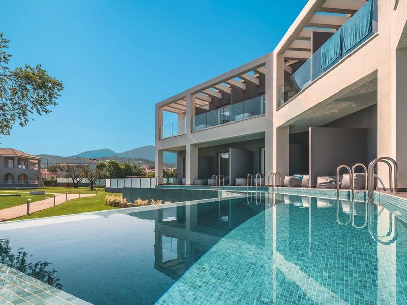 Moderní hotelový bazén s čistou vodou a zahradou za slunečného nebe.