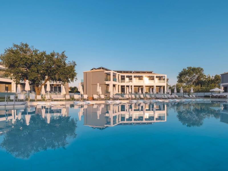 Moderní hotelový komplex s bazénem a hustými stromy pod jasnou oblohou.