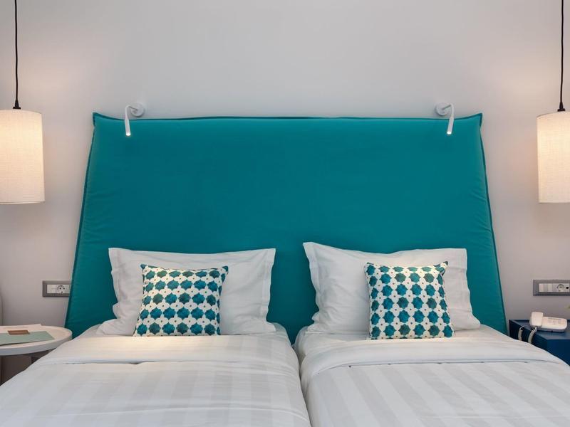 Dvě jednolůžka s tyrkysovým čelem a dekorativními polštáři v hotelovém pokoji.