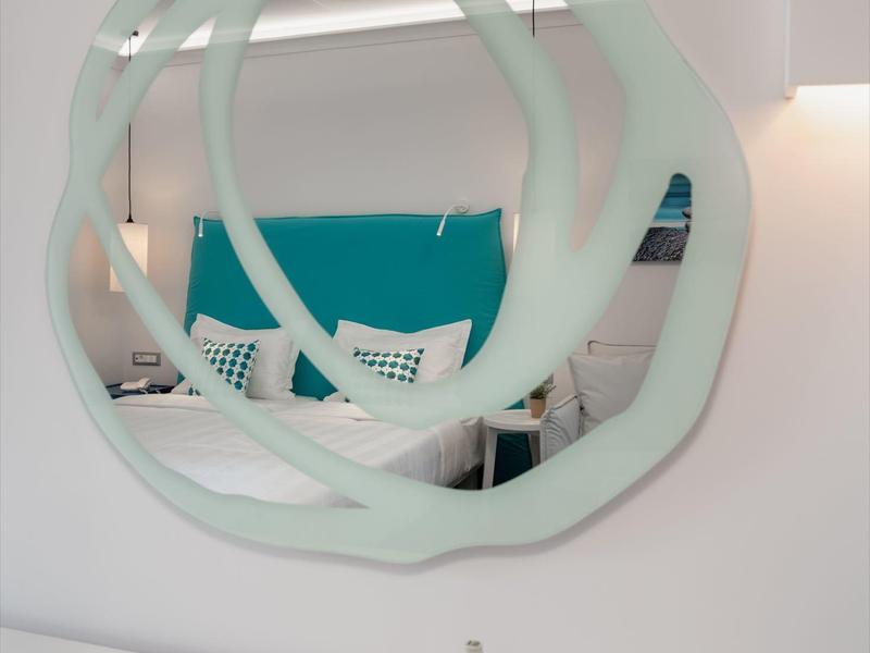 Moderní zrcadlo s vlnitým okrajem nad psacím stolem s lahví vody v hotelovém pokoji.