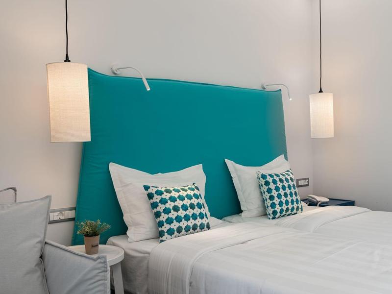 Moderní hotelový pokoj s tyrkysovým čelem postele, bílými postelemi a závěsnými lampami.