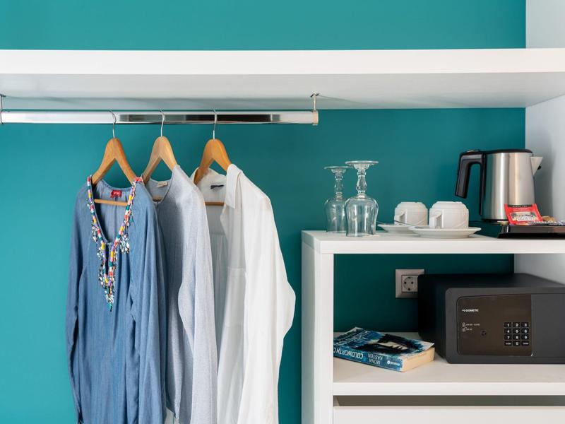 Hotelový pokoj s župany, sejfem, varnou konvicí a sklenicemi před tyrkysovou stěnou