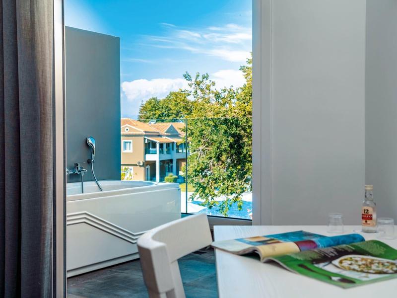 Moderní hotelový balkon se stolem, židlí a výhledem na bazén a budovu.