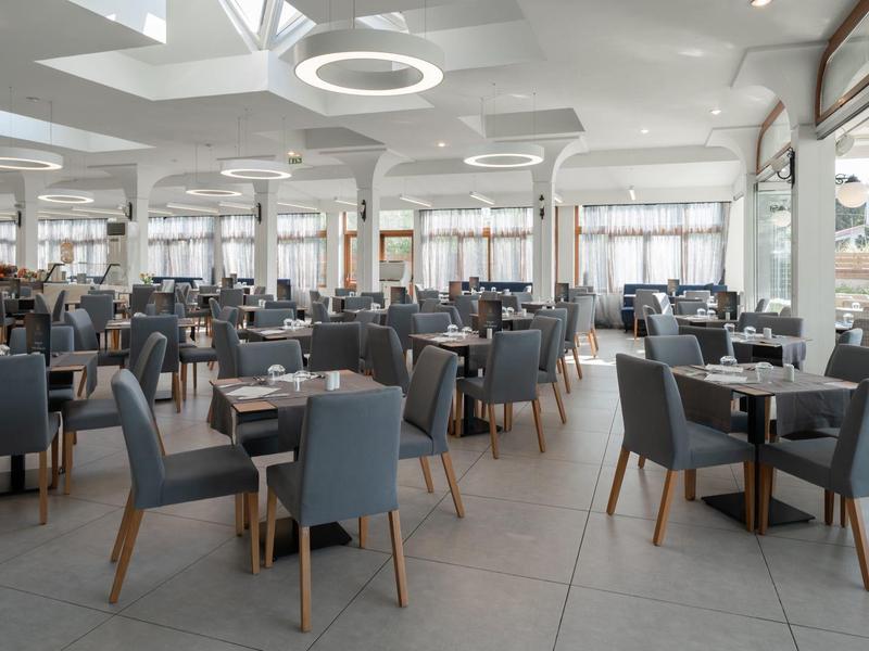 Velká moderní jídelna s modrými židlemi a bílými stoly v hotelu.
