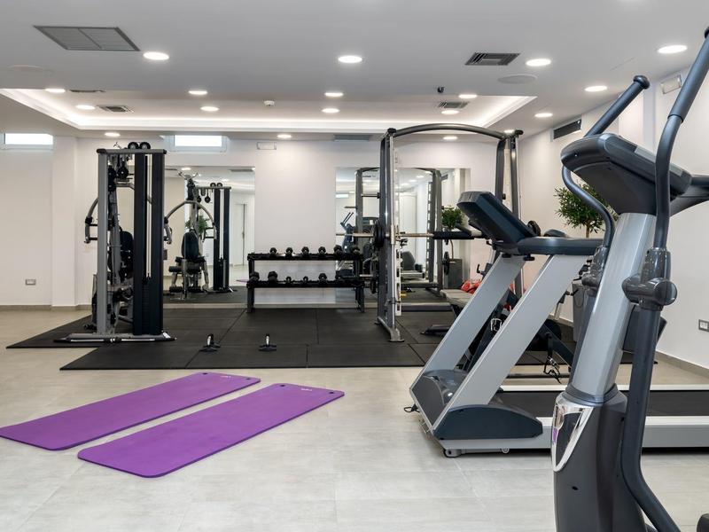 Moderně vybavená posilovna s běžeckým pásem, tréninkovými stroji a dvěma fialovými jógovými podložkami.