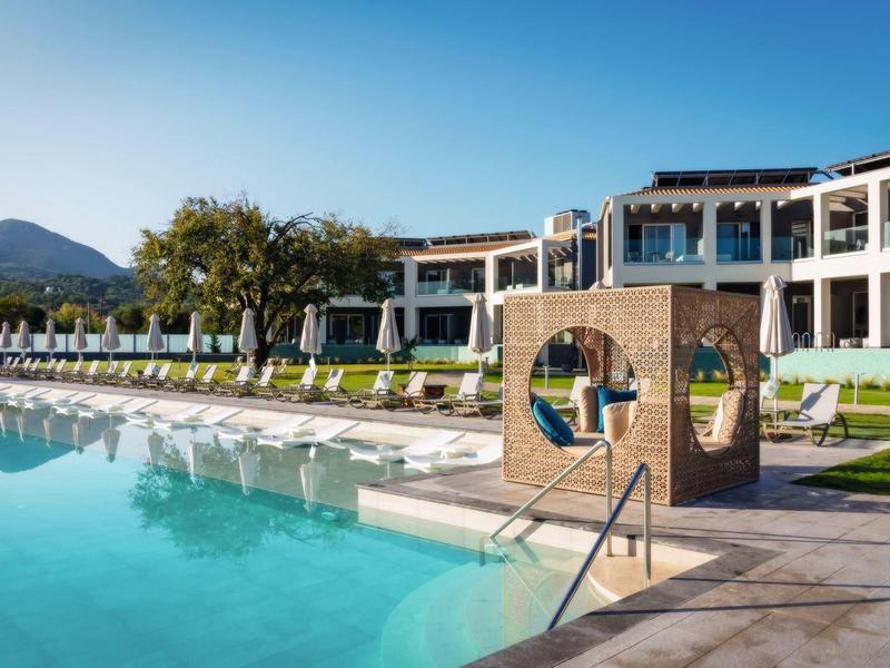 Hotel s velkým bazénem, lehátky a výhledem na hory za jasné oblohy.