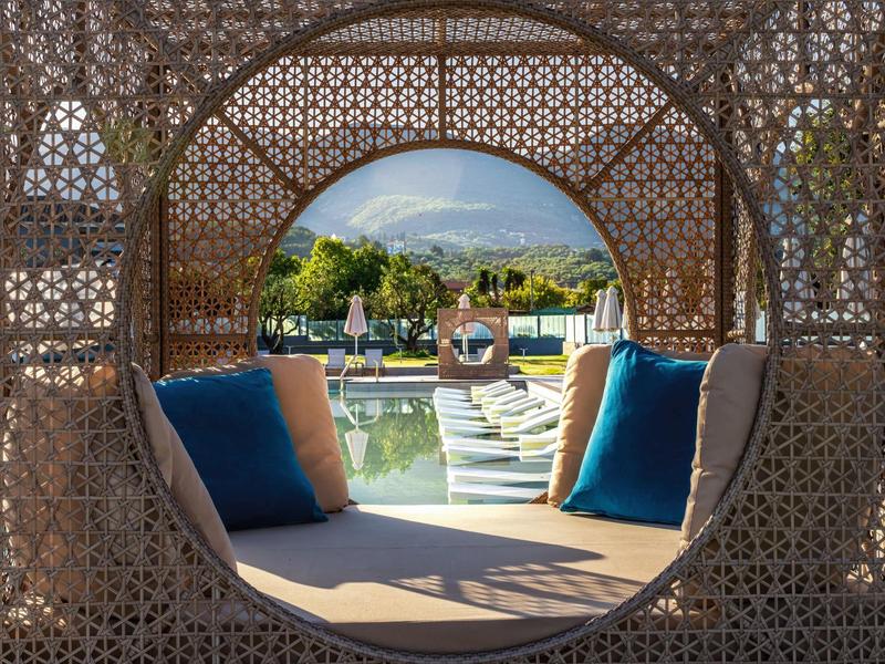 Pohodlný lounge s kruhovým otvorem, výhled na bazén a lehátka v hotelové zahradě.