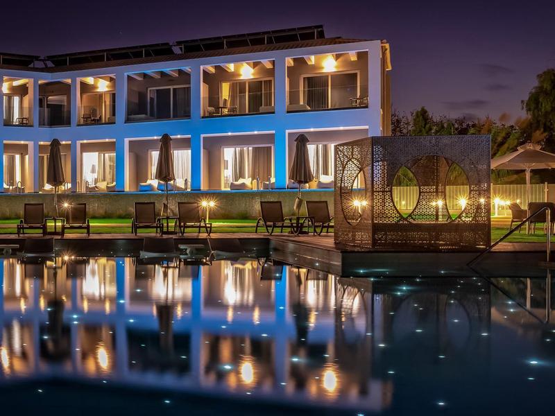 Moderní hotel s osvětleným bazénem a odrazy v noci.