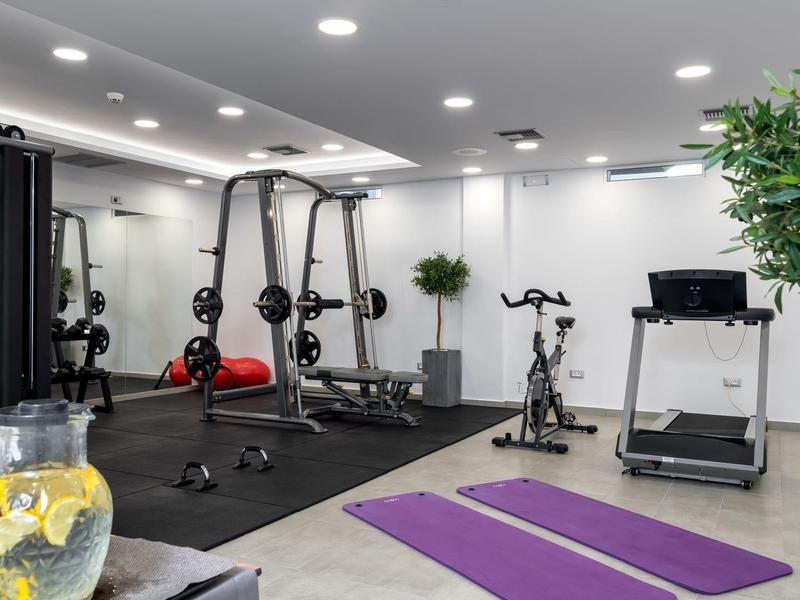 Světelné fitness s posilovacími stroji, podložkami na jógu a dekorativními rostlinami.