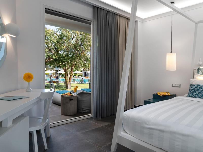 Moderní hotelový pokoj s bílým nábytkem a přístupem na terasu s posezením