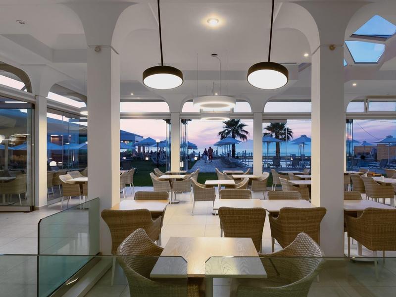 Moderní restaurace s výhledem na palmy a moře při západu slunce.