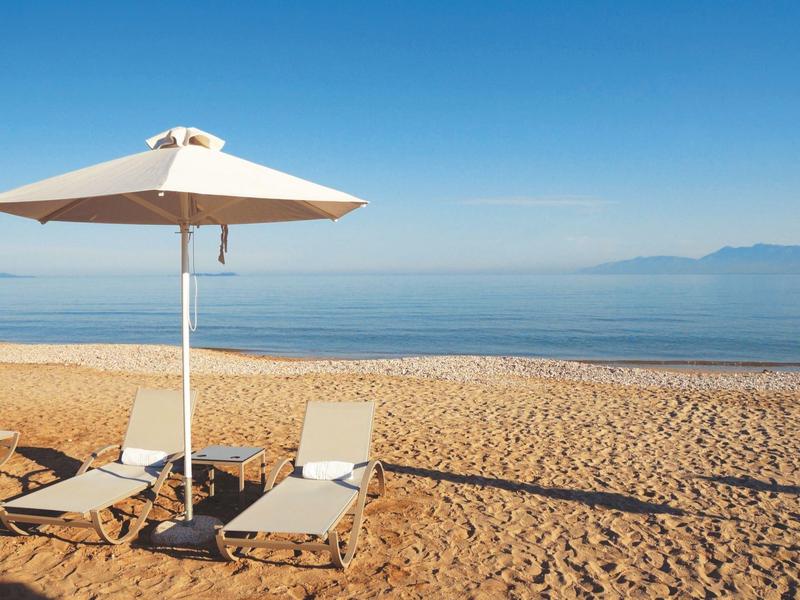 Pláž se dvěma lehátky pod bílým slunečníkem za jasné oblohy