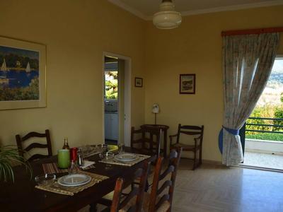 Sala da pranzo con tavolo in legno, sedie, tavola apparecchiata e vista su una terrazza con ringhiera.