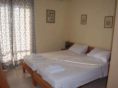 Camera d'hotel luminosa con due letti singoli, biancheria bianca e asciugamani piegati vicino a una finestra con tende.