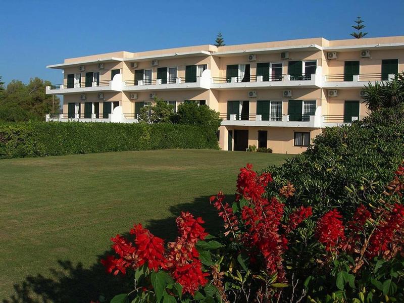 Dvoupodlažní hotelová budova s balkony a upravenou zahradou s červenými květinami v popředí.