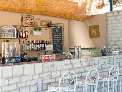 Acogedor bar con pared de piedra, mostrador alto, sillas blancas y bebidas en estantes.