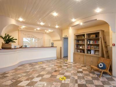 Luminosa recepción de hotel con mostrador, estantería de libros y silla moderna sobre suelo de mármol.