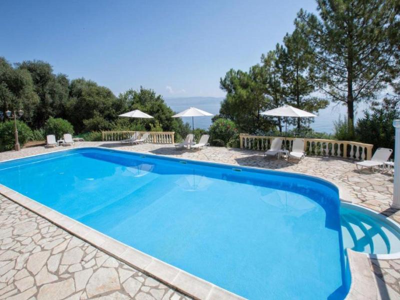 Basen na zewnątrz z leżakami i parasolami, otoczony drzewami i śródziemnomorskim krajobrazem.