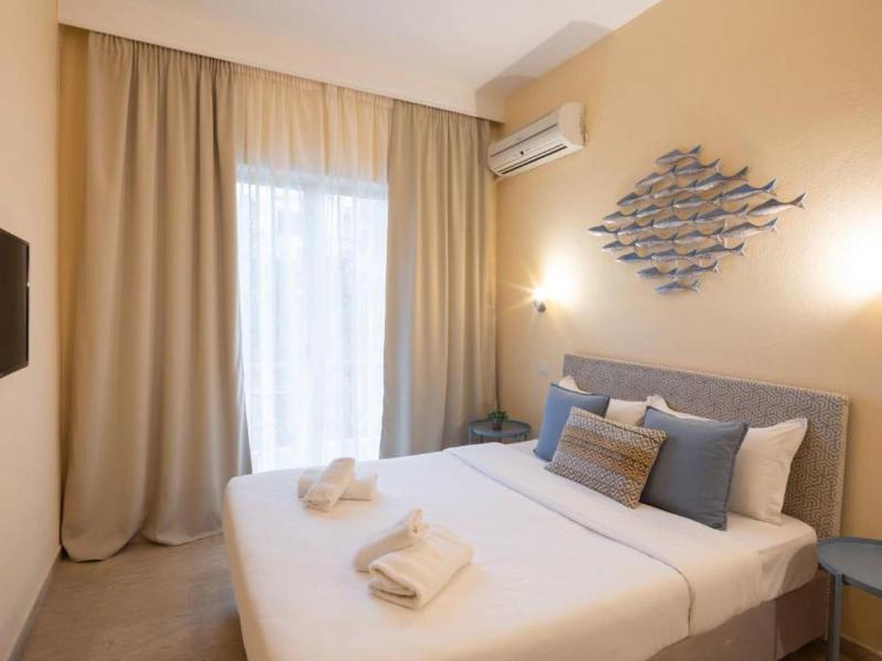 Jasny pokój hotelowy z łóżkiem podwójnym, dwoma ręcznikami, niebiesko-szarymi poduszkami i zasłonami.